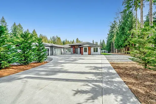 An expansive view of a pristine, freshly pressure-washed concrete driveway leading to a modern luxury residential home surrounded by trees.